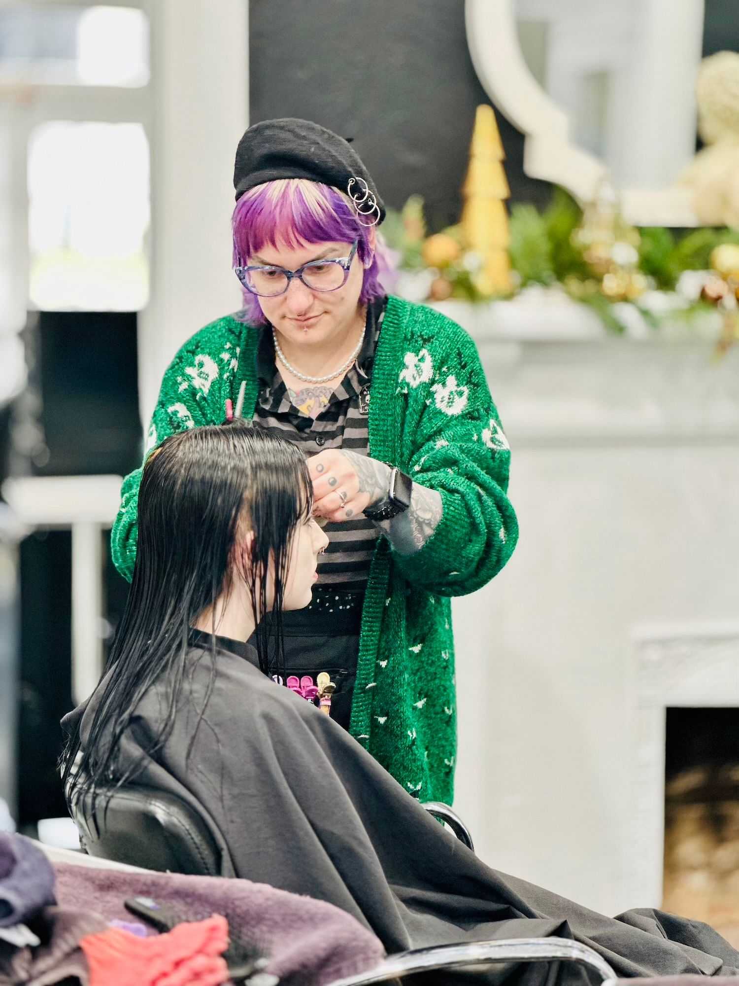 A stylist with purple hair cutting a client's hair in a salon.