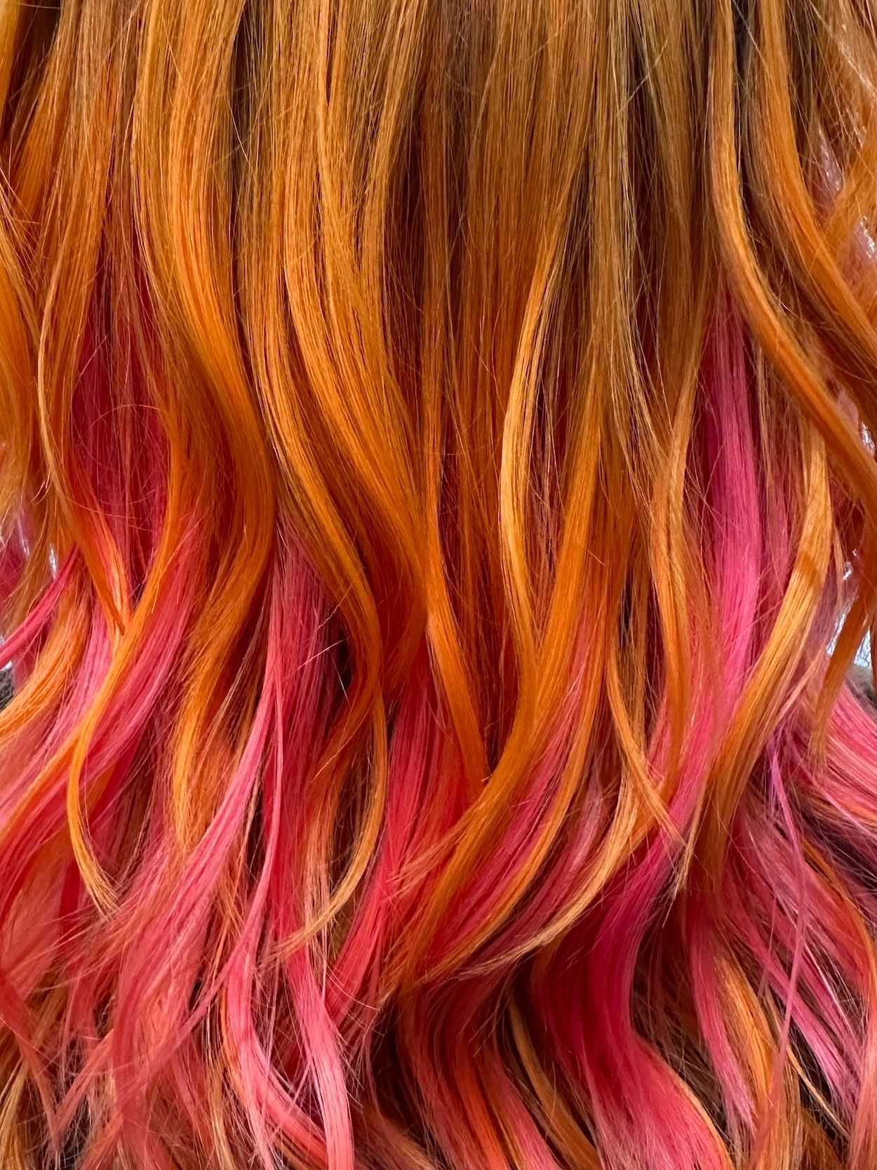 Close-up of vibrant red and orange wavy hair with pink highlights.